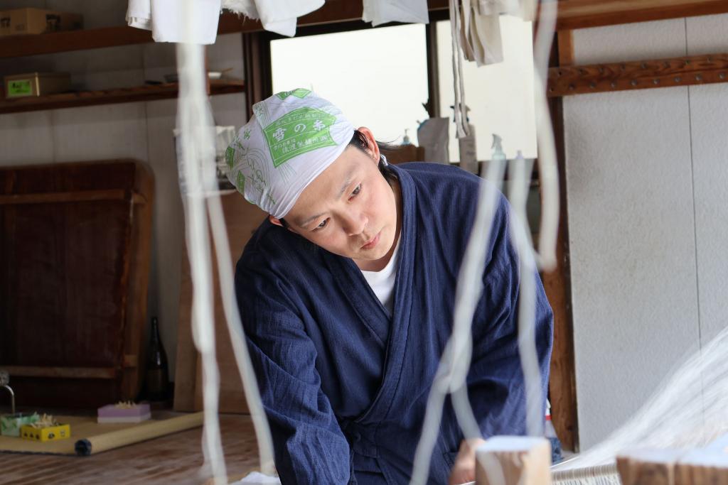 写真：雪の糸ロゴプリントの手ぬぐいを頭に巻いた男性が作業している様子