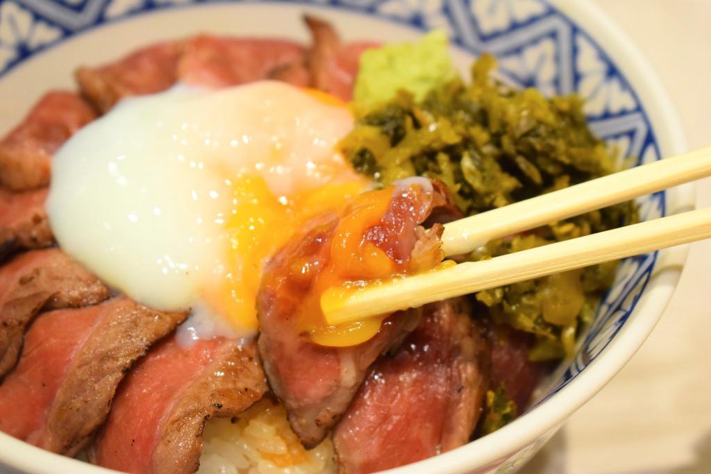 あか牛丼のお肉の切り身に卵黄を合わせて、箸で持ち上げている写真