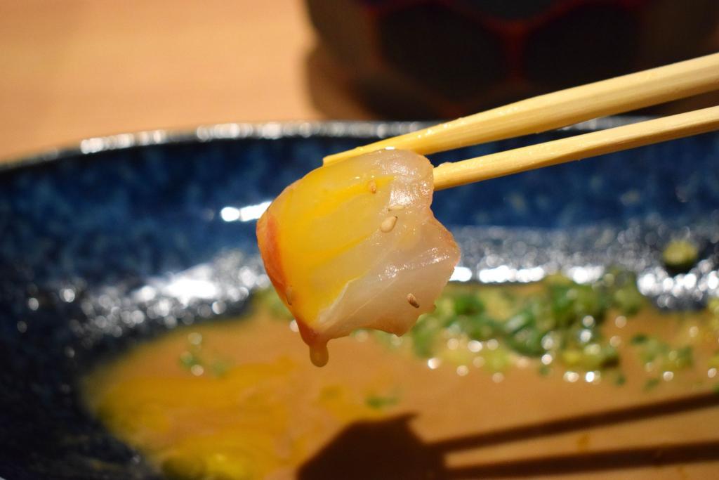 鯛の月見茶漬けご飯と旬野菜天ぷら定食の鯛の切り身を卵黄と絡めて箸で持ち上げている写真