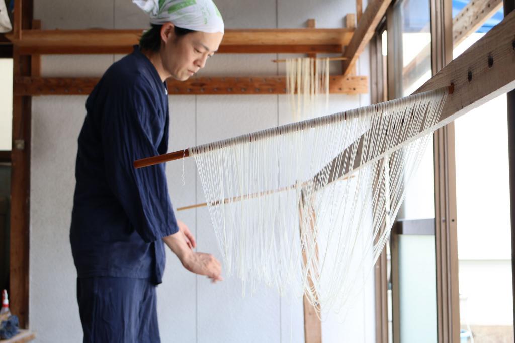 写真：素麺づくりの工程。2本の竿に渡したそうめんをさばいている様子
