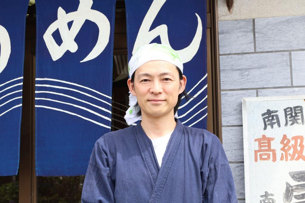 写真：店舗前に立つ師富さん