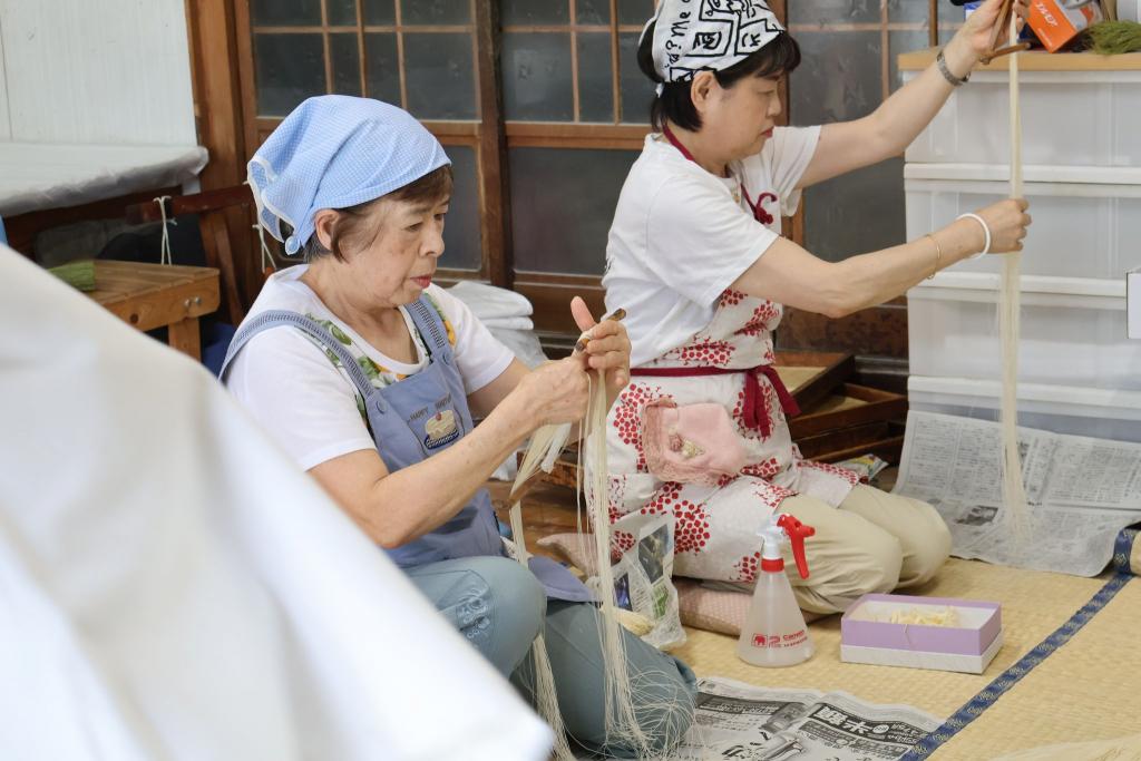 写真：素麺づくりの工程。室内で女性2名が素麺を束ねている様子