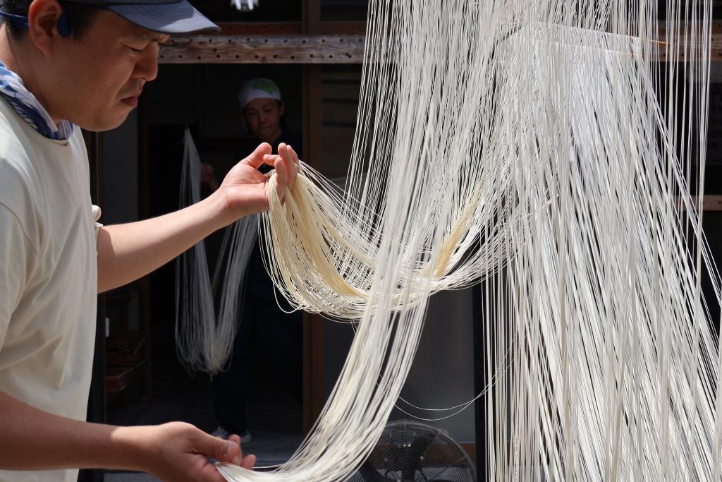 写真：素麺づくりの工程。物干しにかけたそうめんをさばいている様子