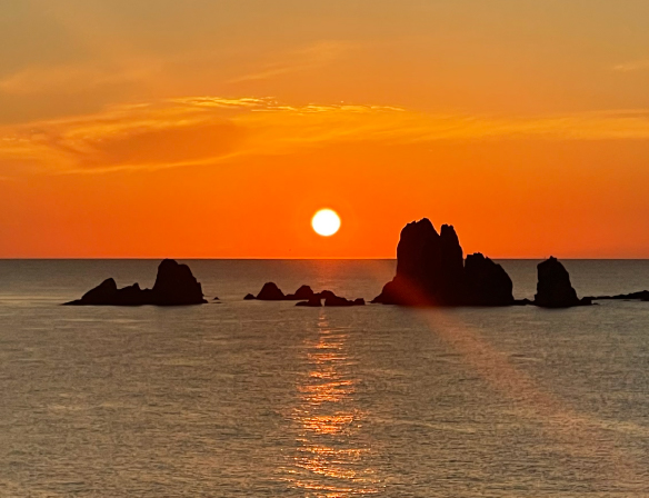 水平線に沈む夕陽と海に浮かぶ岩礁が織りなす風景